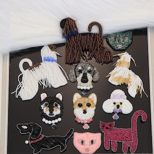 Puede incluir: Una colección de broches de animales hechos con cuentas que presentan varios diseños de perros y gatos. El surtido incluye formas de cuerpo completo y solo de cabeza, elaboradas con cuentas de vidrio en colores como negro, blanco, marrón, rosa y dorado, con algunos dijes.