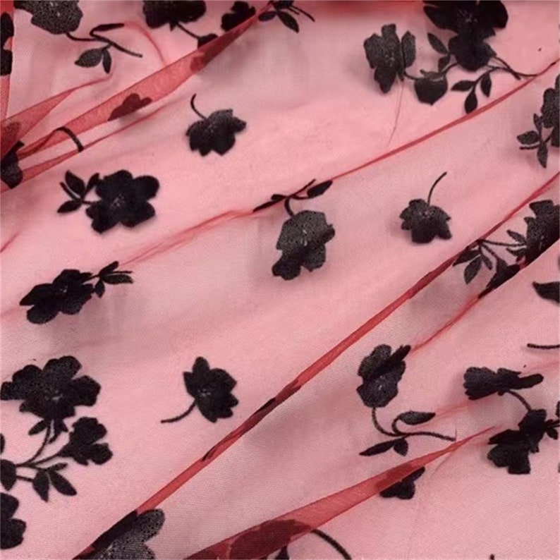 May include: Red sheer fabric with black floral embroidery. The fabric has a delicate, almost translucent quality.
