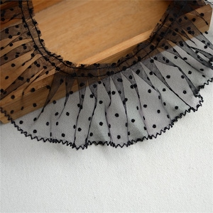 May include: Black lace trim with small white polka dots. The lace has a ruffled edge.