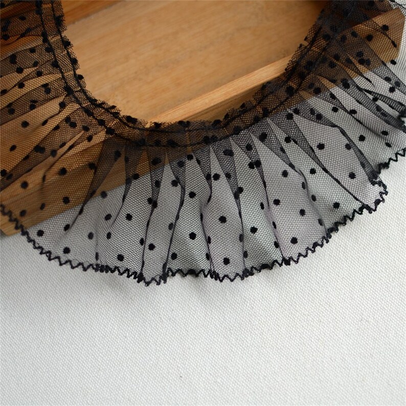 May include: Black lace trim with small white polka dots. The lace has a ruffled edge.