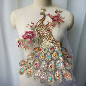May include: Gold and iridescent peacock applique with colorful rhinestones and sequins. The peacock is standing on a floral branch with pink flowers.