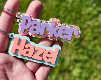 May include: Two colorful acrylic keychains with the names "Parker" and "Hazel" in a bubbly font. The keychains are decorated with colorful confetti.