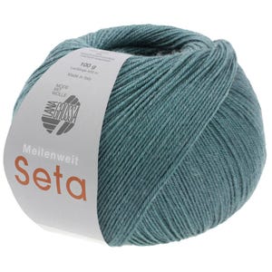 Op de afbeelding: Een bolletje teal garen met een wit etiket. Het etiket leest "Meilenweit Seta" en bevat het merklogo en details over het gewicht van het garen, dat 100 g is. Het garen is gemaakt in Italië.