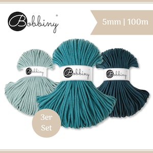 Pode incluir: Um conjunto de três bobinas de cordão Bobbiny em tons de azul claro, azul-petróleo e azul escuro. Cada bobina está rotulada como 5mm | 100m e apresenta o logótipo da marca Bobbiny numa faixa de papel branco. O conjunto é apresentado como 3er Set.