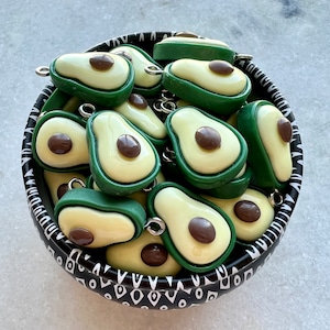 May include: A bowl filled with green and brown avocado-shaped charms with silver jump rings. The bowl has a black and white geometric pattern.