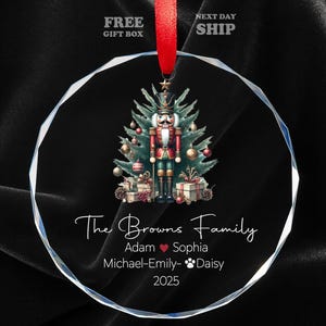 May include: A clear, round Christmas ornament with a red ribbon. The ornament features a detailed illustration of a nutcracker soldier in front of a Christmas tree. Text on the ornament reads "The Browns Family", names, and the year 2025.