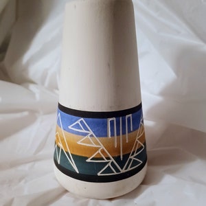 May include: White ceramic vase with a geometric design in blue, yellow, and green. The vase is cone-shaped and has a narrow opening.