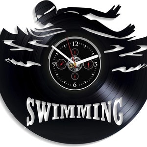 Op de afbeelding: Een zwarte vinyl platenspeler klok met een silhouet van een zwemmer in het water. De wijzerplaat van de klok heeft een zwarte achtergrond met witte cijfers en wijzers. De klok is gelabeld "SWIMMING".