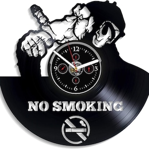 May include: A black vinyl record clock with a white silhouette of a person smoking a cigarette. The clock face is black with white numbers and hands. The text "NO SMOKING" is printed in white on the record. A no smoking symbol is printed below the text.