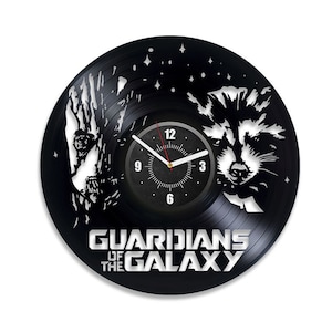 Pode incluir: Relógio de vinil preto com uma silhueta de Rocket Raccoon e Groot do filme Guardiões da Galáxia. O mostrador do relógio é preto com números e ponteiros brancos.