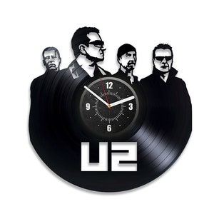 Op de afbeelding: Een zwarte vinyl platenspeler klok met de band U2. De wijzerplaat van de klok is wit met zwarte cijfers en wijzers. De bandleden zijn in zwart gesilhouetteerd rond de wijzerplaat van de klok.