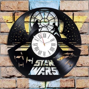 May include: A black vinyl record clock featuring a silhouette of Darth Vader and Luke Skywalker facing each other in a lightsaber duel. The clock face is white with black Roman numerals and a red hour hand. The words "Star Wars" are printed in black below the clock face.