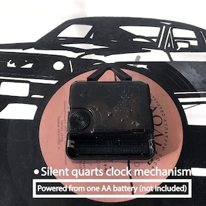 May include: Black vinyl record clock featuring a silhouette of a car. The clock mechanism is visible on the back of the record. The text "Silent quarts clock mechanism" and "Powered from one AA battery (not included)" is printed on the record.