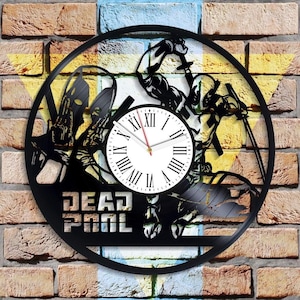 Può includere: Orologio in vinile nero con una silhouette di Deadpool che tiene una katana. Il quadrante dell'orologio è bianco con numeri romani neri. Le parole "DEAD POOL" sono stampate sotto il quadrante dell'orologio.