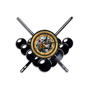 Könnte beinhalten: Eine schwarz-goldene Wanduhr mit Billard-Motiv. Das Zifferblatt zeigt sichtbare Zahnräder und römische Ziffern. Zwei gekreuzte Billardqueues und eine Ansammlung schwarzer Billardkugeln vervollständigen das Design.