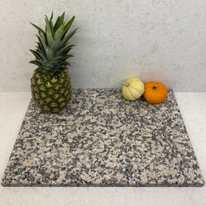 May include: A gray granite cutting board with a speckled pattern. A pineapple and two small pumpkins are on the board.