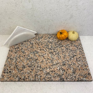 May include: A pink and gray granite cutting board with a white napkin holder and two small pumpkins, one orange and one white.