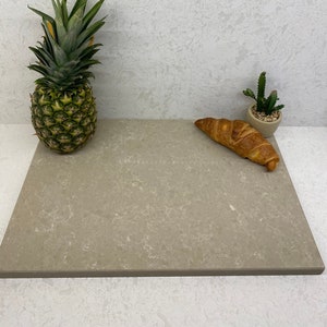 May include: A light beige countertop with a pineapple and a croissant on it. The countertop has a speckled pattern.