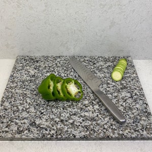 May include: A gray granite cutting board with a green bell pepper sliced and a zucchini sliced on the board. A silver knife is on the board.