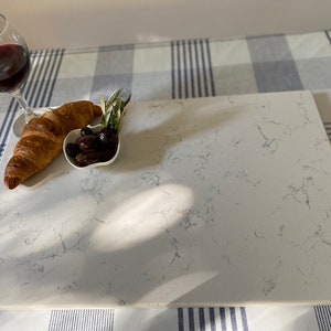 May include: A white marble serving board with a croissant, olives, and a glass of red wine. The board is on a checkered tablecloth.