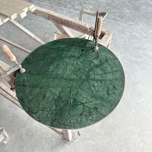 May include: A round, green marble tabletop with a veined pattern. The tabletop is being clamped to a wooden surface.