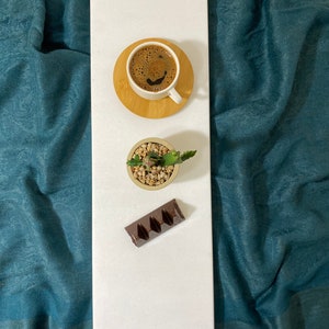 May include: A white rectangular serving tray with a cup of coffee, a small potted succulent plant, and a chocolate bar.