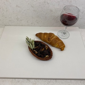 May include: A white rectangular serving tray with a croissant, a small bowl of dried fruit, and a glass of red wine.