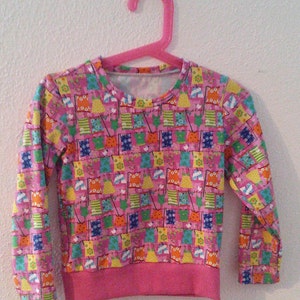 Könnte beinhalten: Rosa Langarmshirt mit einem bunten Muster aus Wäsche, die an einer Wäscheleine hängt.