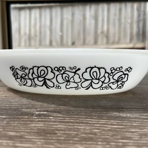 May include: White oval casserole dish with a black floral pattern around the rim. The dish has a simple, elegant design, ideal for serving food. The floral design adds a touch of vintage charm to the kitchen.