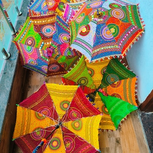May include: A collection of colorful, decorative umbrellas with intricate patterns. The umbrellas feature a variety of bright colors, including red, yellow, green, and blue, with detailed embroidery and fringe trim. The umbrellas are open and displayed on a wooden surface.