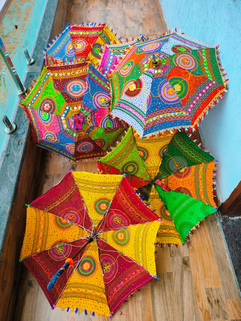 May include: A collection of colorful, decorative umbrellas with intricate patterns. The umbrellas feature a variety of bright colors, including red, yellow, green, and blue, with detailed embroidery and fringe trim. The umbrellas are open and displayed on a wooden surface.