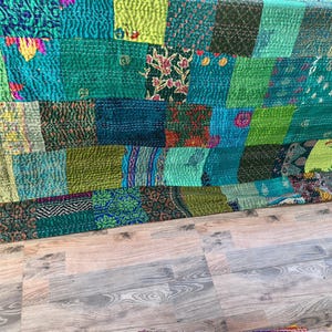 May include: A patchwork textile featuring a variety of green and teal fabrics. The textile is composed of numerous rectangular and square patches, each with unique patterns and textures. The stitching is visible, adding to the handmade aesthetic.