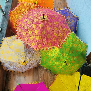 May include: A collection of colorful, decorative umbrellas. The umbrellas feature intricate gold floral patterns on a variety of colored backgrounds, including pink, orange, green, yellow, and blue. Each umbrella has a decorative fringe.