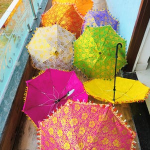 May include: A collection of colorful, decorative umbrellas. The umbrellas are open, showcasing vibrant hues of pink, yellow, green, orange, and purple. Each umbrella features a floral pattern and decorative fringe along the edges.