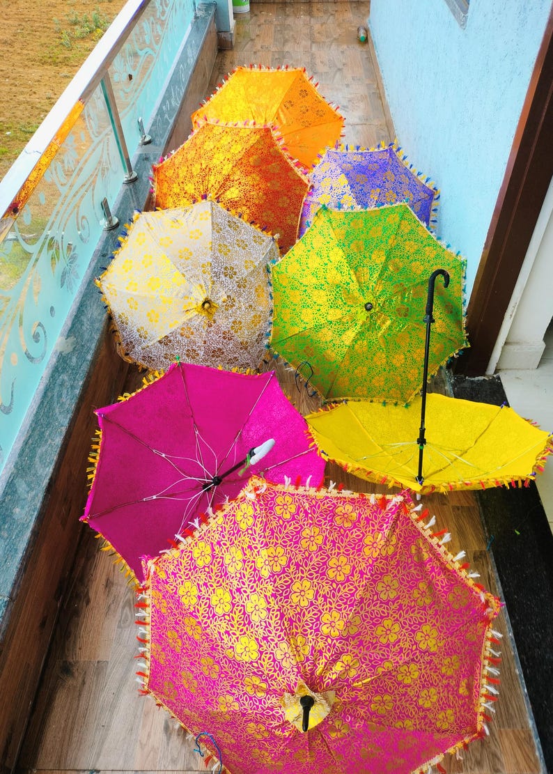 May include: A collection of colorful, decorative umbrellas. The umbrellas are open, showcasing vibrant hues of pink, yellow, green, orange, and purple. Each umbrella features a floral pattern and decorative fringe along the edges.