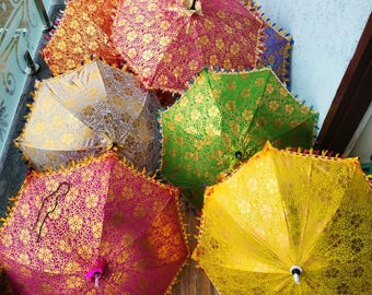 May include: A collection of colorful, open parasols with intricate gold floral patterns. The parasols are in shades of pink, orange, yellow, green, and silver, with decorative fringe around the edges. The parasols are arranged on a wooden surface.