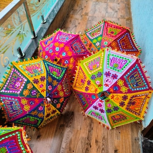 May include: A collection of colorful, hexagonal decorative umbrellas. Each umbrella features a vibrant patchwork design with floral and geometric patterns in shades of pink, green, yellow, and orange. The edges are trimmed with tassels.