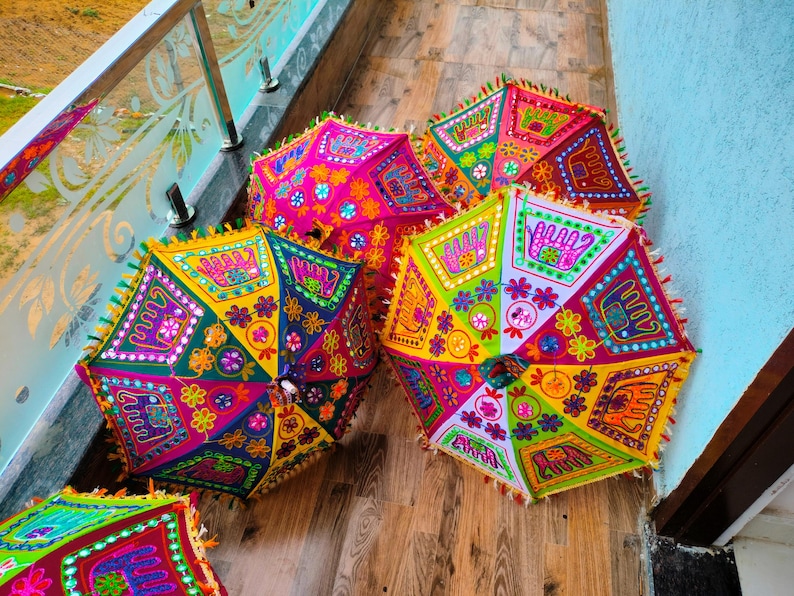 May include: A collection of colorful, hexagonal decorative umbrellas. Each umbrella features a vibrant patchwork design with floral and geometric patterns in shades of pink, green, yellow, and orange. The edges are trimmed with tassels.