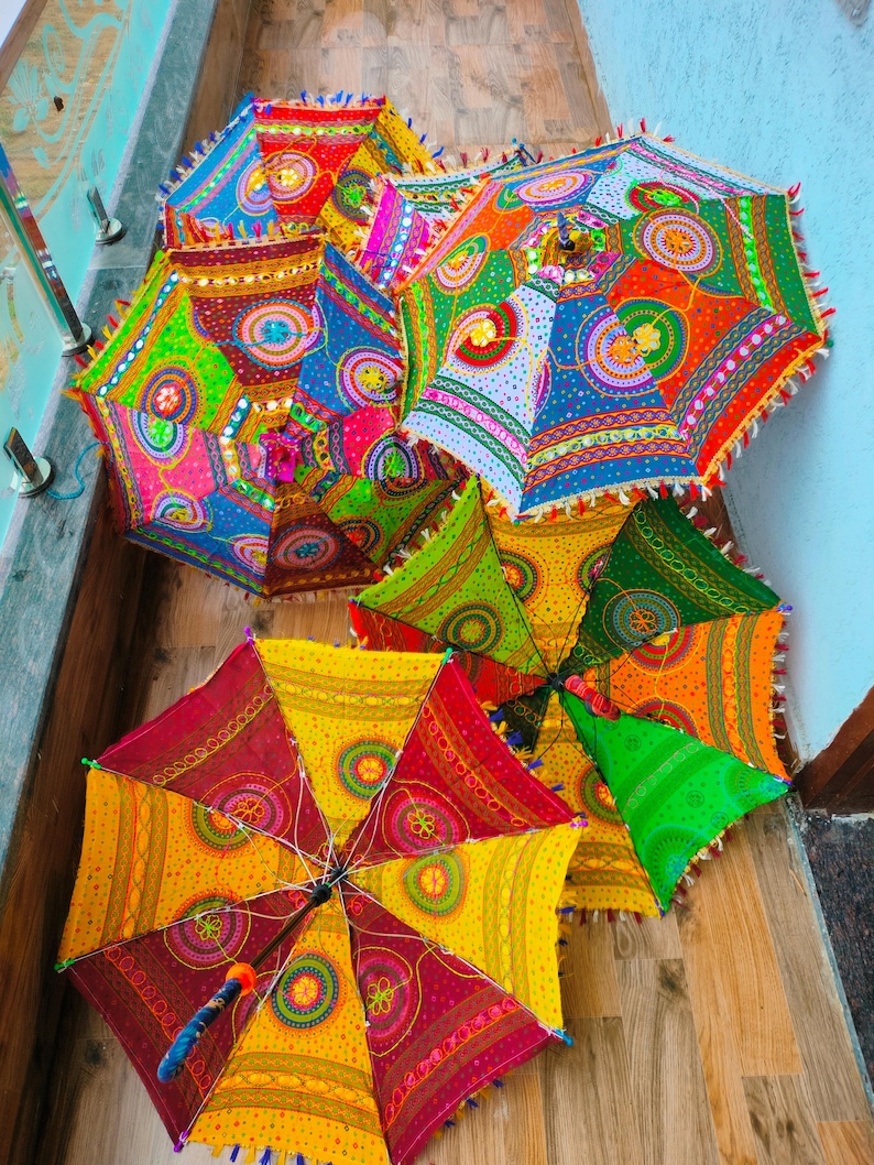 May include: A collection of colorful, decorative umbrellas with intricate patterns. The umbrellas feature a variety of bright colors, including red, yellow, green, and blue, with detailed designs and fringe trim. The umbrellas are open and arranged on a wooden surface.