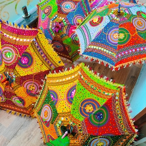May include: A collection of colorful, patterned umbrellas. Each umbrella features a vibrant patchwork design with red, yellow, green, and blue hues. The edges are trimmed with tassels and small mirrors, creating a festive and decorative look.