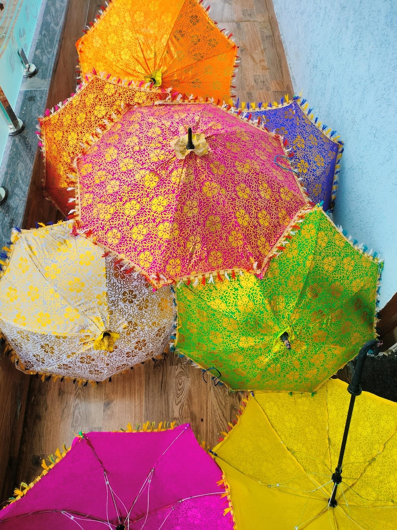 May include: A collection of colorful, decorative umbrellas. The umbrellas feature intricate gold floral patterns on a variety of vibrant backgrounds, including pink, orange, green, yellow, and blue. Each umbrella has a decorative fringe.