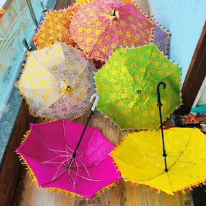 May include: A collection of colorful, decorative umbrellas with intricate floral patterns. The umbrellas are in various shades, including pink, yellow, green, and orange, and are trimmed with tassels. The handles are black or white.
