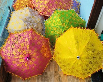 May include: A collection of colorful, decorative umbrellas with intricate floral patterns. The umbrellas are in shades of pink, yellow, green, and orange, with gold accents and tassel trim. The umbrellas are open and arranged on a wooden surface.