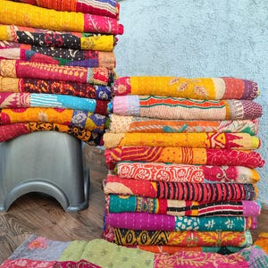 May include: Stacks of colorful, patterned quilts in various sizes. The quilts feature a patchwork design with vibrant hues of red, yellow, pink, and blue. The quilts are folded and stacked, showcasing the intricate stitching and diverse patterns.