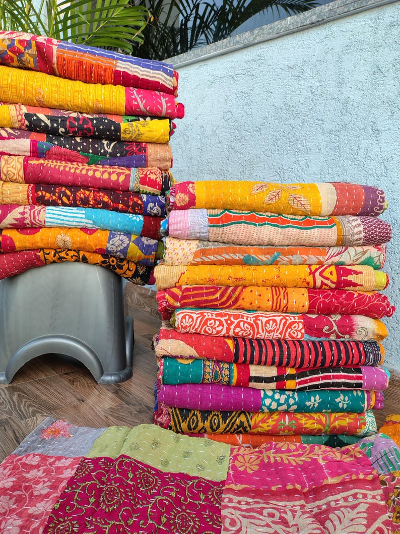 May include: Stacks of colorful, patterned quilts in various sizes. The quilts feature a patchwork design with vibrant hues of red, yellow, pink, and blue. The quilts are folded and stacked, showcasing the intricate stitching and diverse patterns.