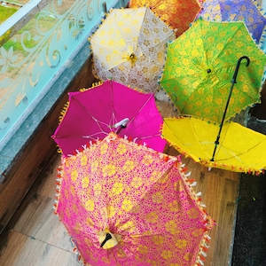May include: A selection of decorative umbrellas in various colours. The umbrellas display bright shades of pink, yellow, green, orange, and blue, with detailed floral designs and tassel edging. Some are open, others closed.