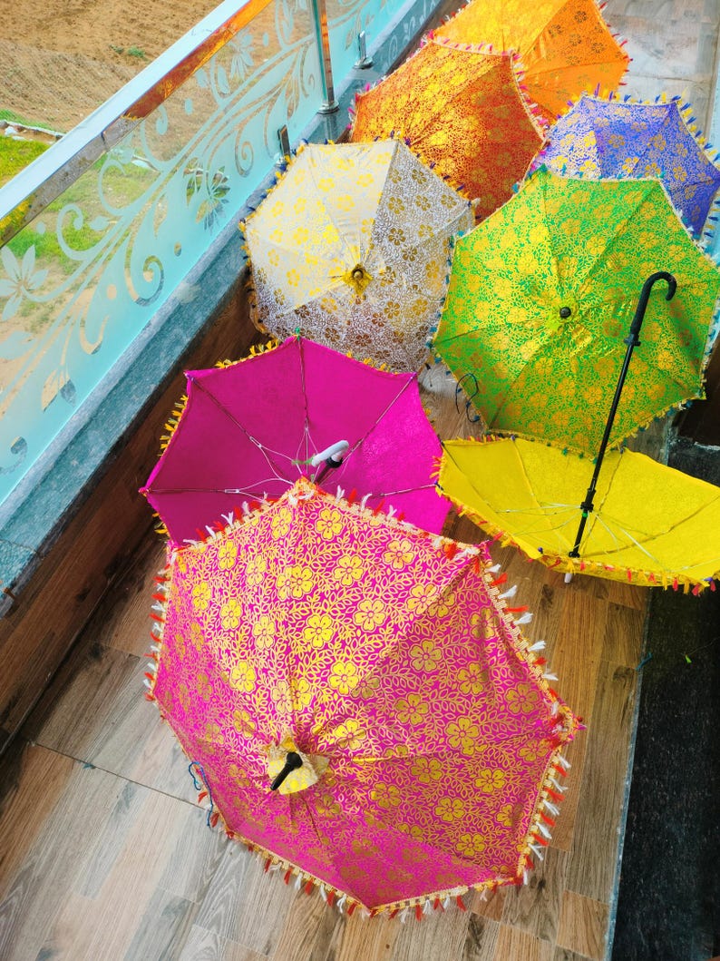 May include: A collection of colorful, decorative umbrellas. The umbrellas feature vibrant hues of pink, yellow, green, orange, and blue, with intricate floral patterns and tassel trim. Some umbrellas are open, while others are closed.