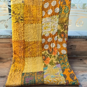 May include: A patchwork quilt with a variety of yellow and gold fabrics. The quilt features floral, polka dot, and textured patterns, stitched together with white thread. The quilt is displayed on a wooden surface.