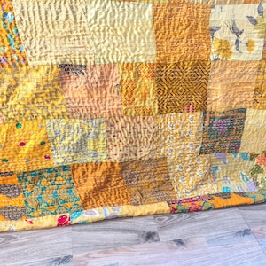 May include: A patchwork quilt with a variety of warm colors, including yellow, orange, and gold. The quilt is made of different fabric squares with various patterns and textures, creating a cozy and inviting look.