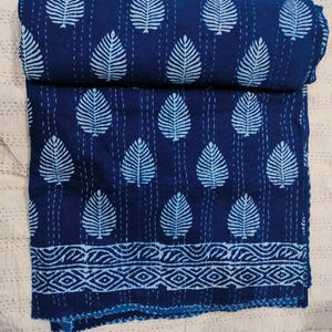May include: A blue and white kantha quilt with a leaf pattern. The quilt is folded in half and has a decorative border.